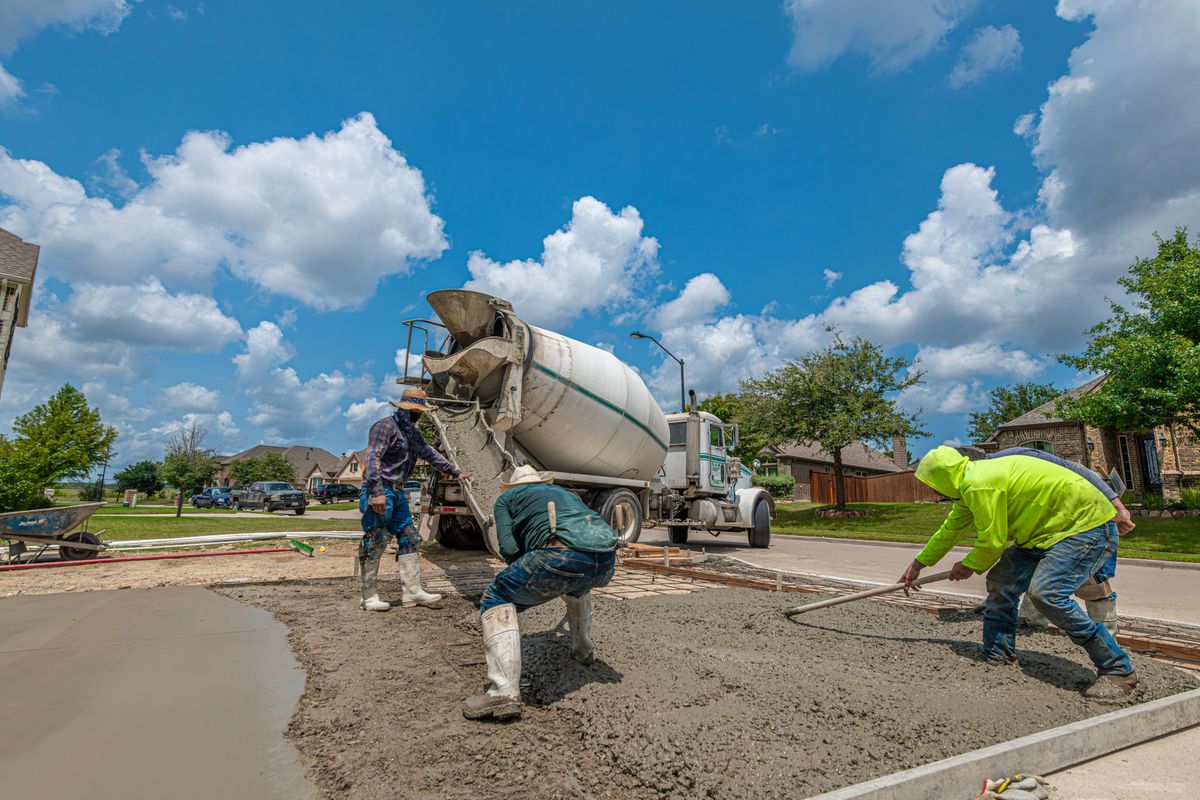 Crew spreading and screeding fresh concrete for a residential driveway as a mixer truck discharges its load.