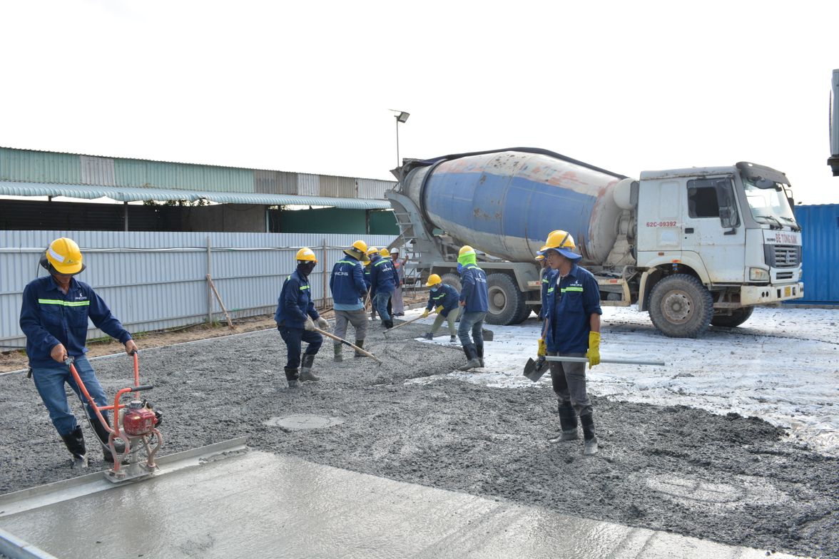 Workers in safety gear placing concrete from a ready-mix truck during a flatwork pour.