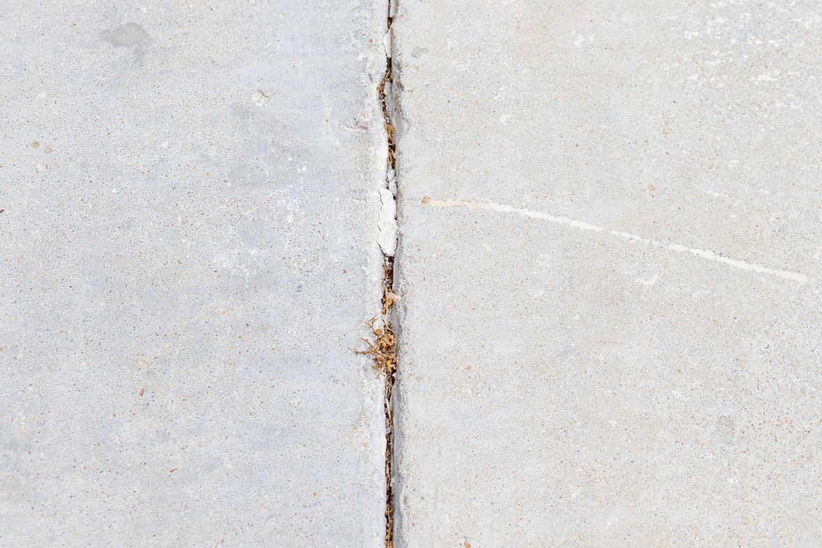 Cracking and spalling along the control joint of an aging concrete walkway.